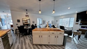 A spacious kitchen with a central island, wooden flooring, pendant lighting, and a view of the outdoors through large windows. - 37PA Superbly appointed riverfront home in LIttleton! Skiing, hiking, firepit, wifi, dog friendly! (Littleton)