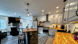 A modern kitchen with a central island, wooden flooring, and white cabinetry. - 37PA Superbly appointed riverfront home in LIttleton! Skiing, hiking, firepit, wifi, dog friendly! (Littleton)