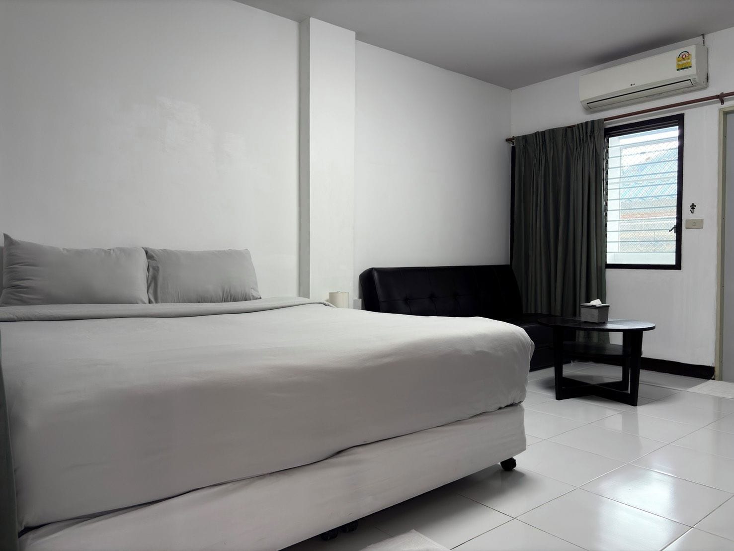 A hotel room with a bed, a chair, a small table, and a window with curtains.