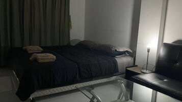 A bedroom with a bed, pillows, a bedside table, a lamp, and a glass table with chairs.