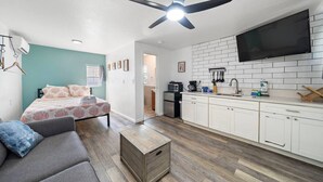 A bedroom with a bed, a gray sofa, a wooden chest, and a ceiling fan. - Cozy Oceanview Studio on Galveston’s East End (Galveston)