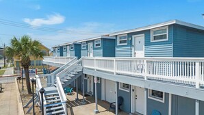 A coastal cottage with a balcony, a staircase, and a sign for Coastal Cottages by Beach Box.