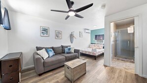 A modern living room with a grey sofa, a wooden coffee table, a ceiling fan, and a glass shower door.