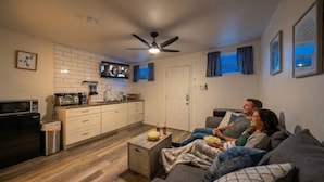 A modern living room with a sofa, a coffee table, a TV, and a kitchen area with cabinets and appliances.