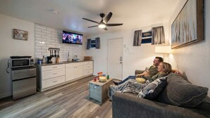 Ein kompakter Wohnbereich mit Küchenzeile, Deckenventilator, Flachbildfernseher und einer Couch.