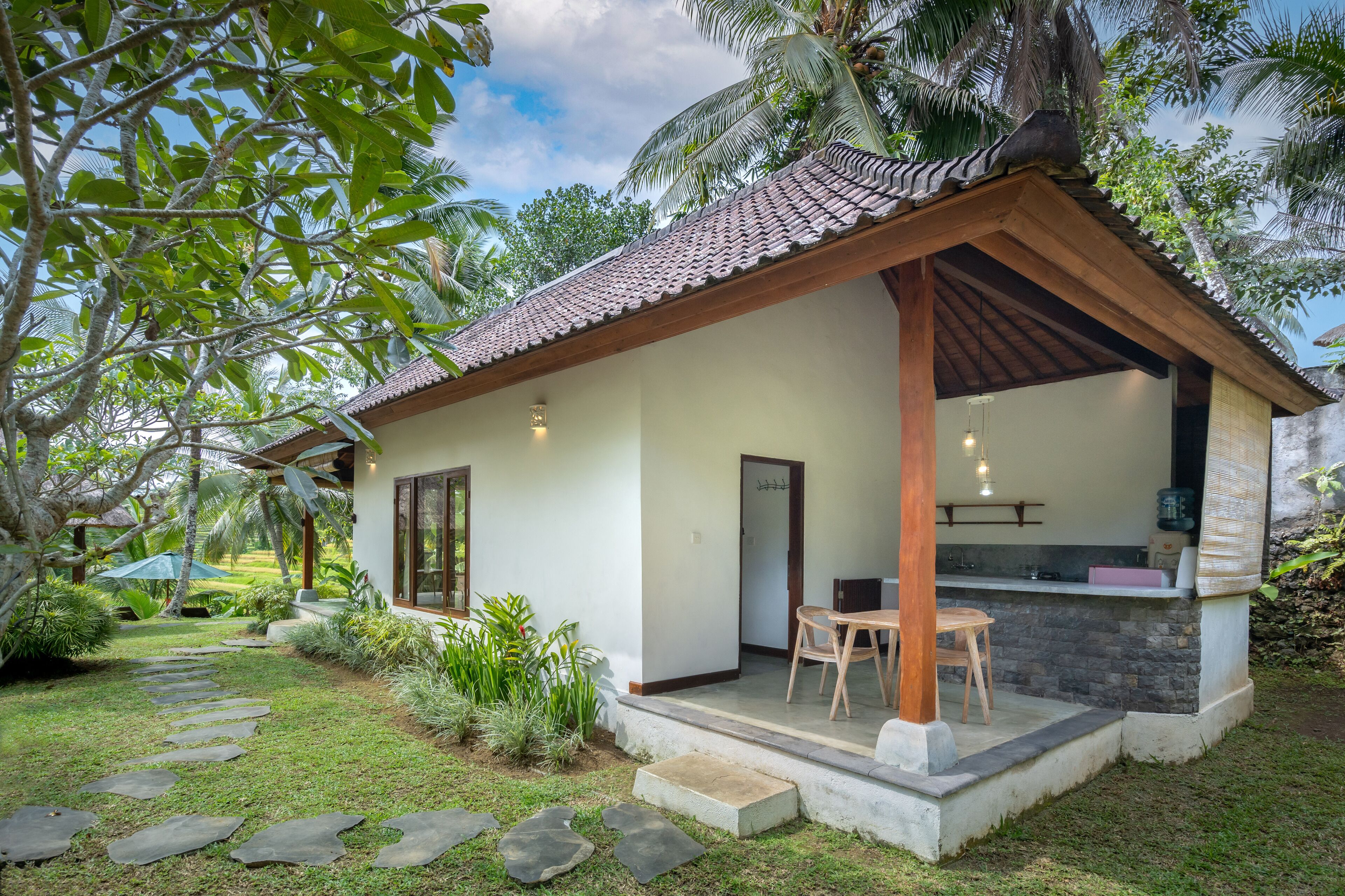 A house with a tiled roof, a porch with a table and chairs, and a stone pathway leading to the entrance.