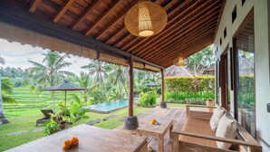 A covered outdoor seating area with wooden furniture and a hanging light fixture. - Green Sari Private Villa (Ubud)