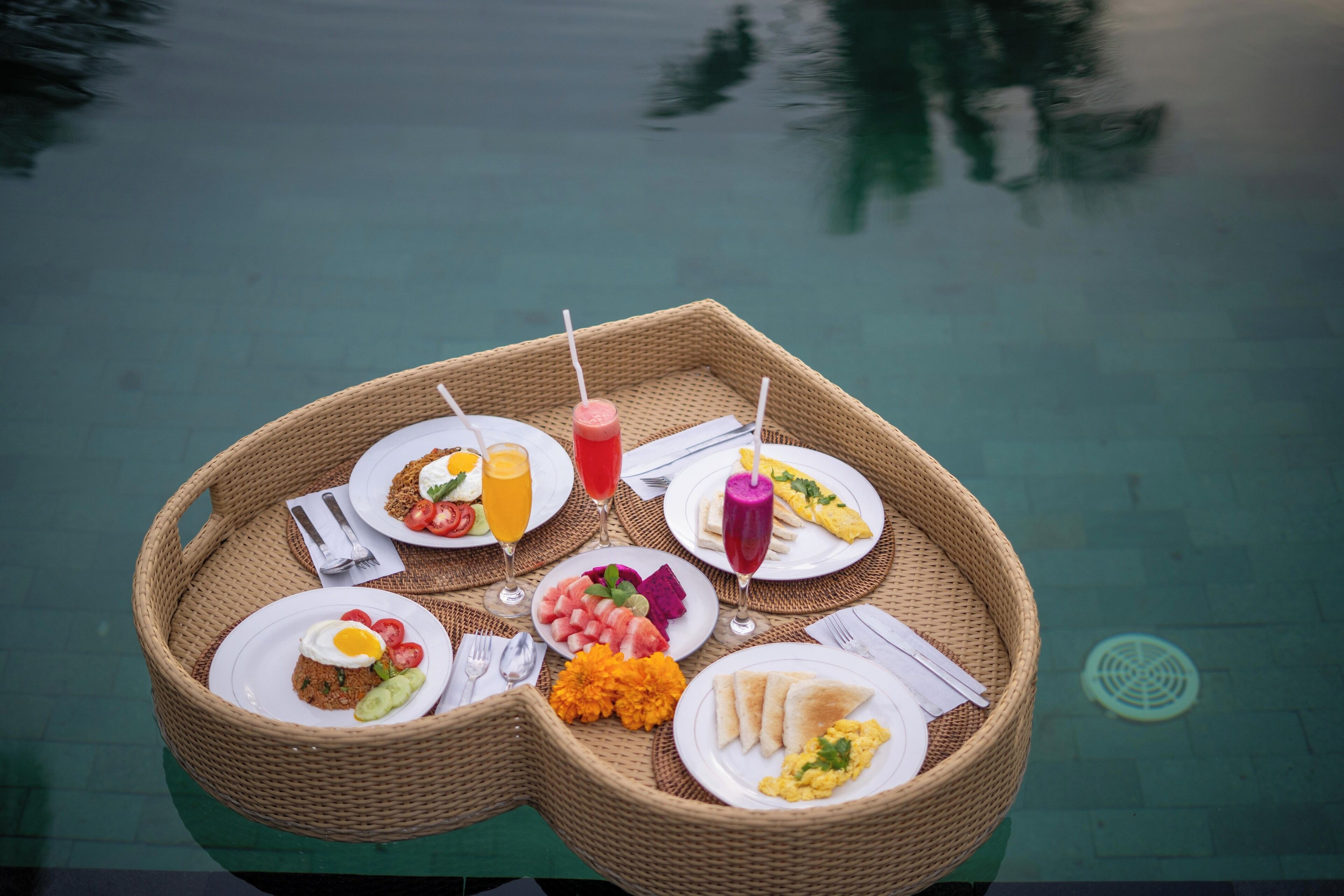 A dining setup on a poolside table with various dishes and drinks.