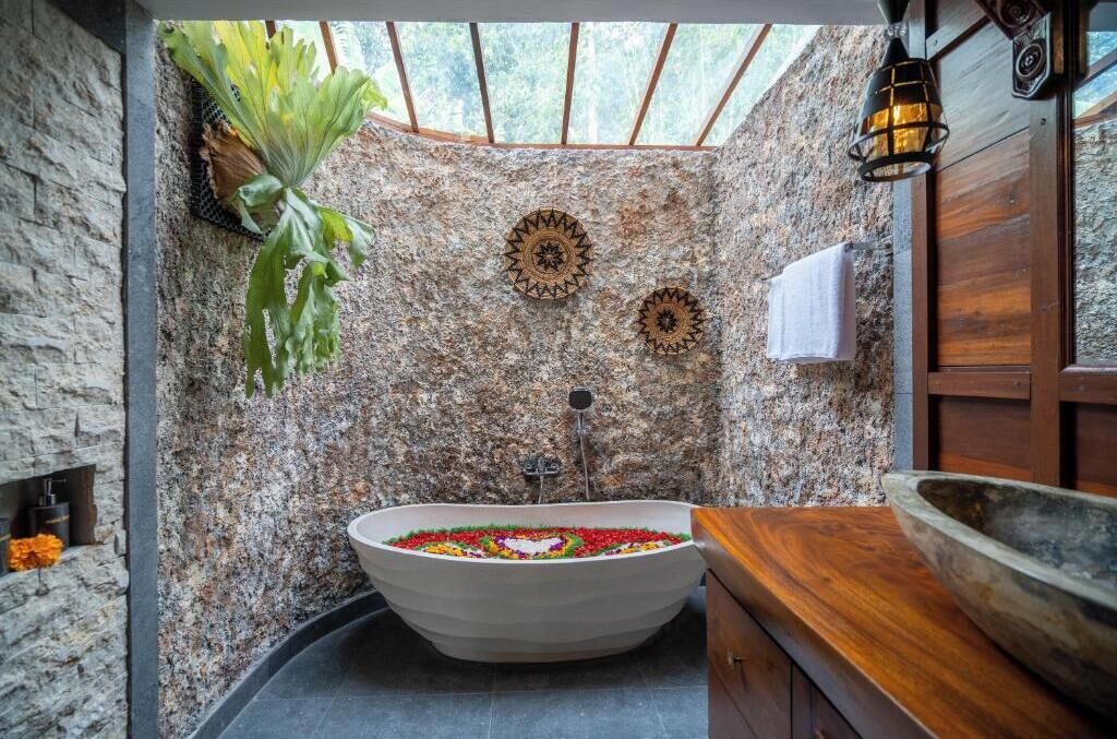 A bathroom with a freestanding bathtub filled with colorful flowers, a stone wall, and a wooden vanity.