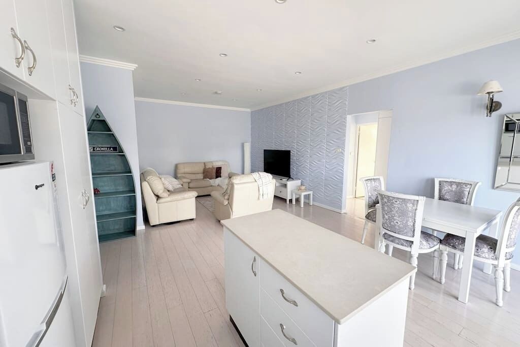 A modern living room with a sofa, a dining table with chairs, a TV, and a staircase leading to a lower level.