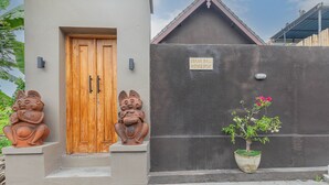 A building with a wooden door, a sign reading "SEKAR BALI HOME STAY", and a potted plant with pink flowers. - Sekar Bali Homestay (Gianyar)