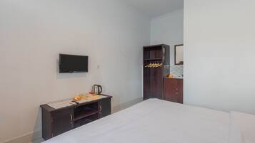 Habitación de hotel con cama, televisor montado en la pared, una pequeña mesa de trabajo con hervidor y armario con espejo.