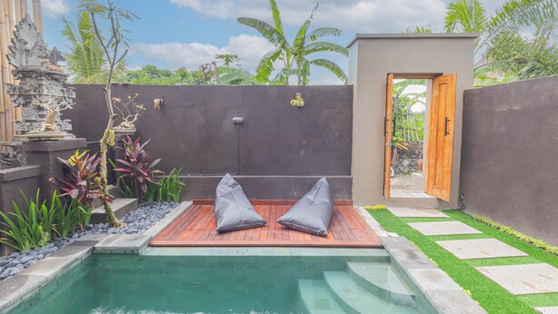 A private pool area with two grey cushions on a wooden deck, surrounded by a low stone wall and lush greenery. - Sekar Bali Homestay (Gianyar)