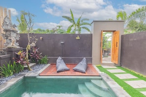 A private pool area with two grey cushions on a wooden deck, surrounded by a low stone wall and lush greenery. - Sekar Bali Homestay (Gianyar)