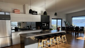 A modern kitchen with a large island, wooden bar stools, and a view of the sea. - Fusion House (Tranmere)