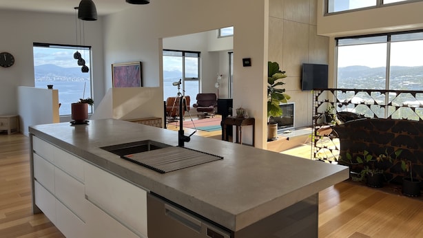 A modern kitchen with a large island, pendant lights, and a view of the sea. - Fusion House (Tranmere)