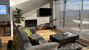 A modern living room with a grey sofa, a flat-screen TV mounted on the wall, a fireplace, and large windows offering a view of the city. - Fusion House (Tranmere)