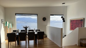 A dining area with a view of a lake and mountains, wooden flooring, and a modern interior design. - Fusion House (Tranmere)