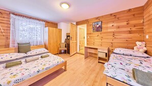 A cozy room with wooden walls, two beds with floral bedding, a desk, and a teddy bear. - Chaloupka U lesa by Interhome (Harrachov)