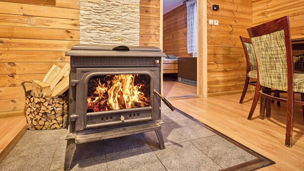 A wood-burning stove in a room with wooden walls and a stone accent wall. - Chaloupka U lesa by Interhome (Harrachov)