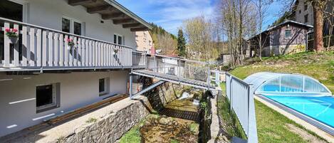 Un edificio con balcón, un pequeño arroyo y una piscina.