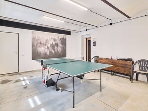Una mesa de ping pong en una habitación con un gran mural de un bosque, un escritorio de madera y dos sillas.