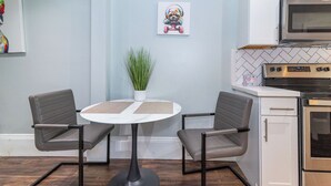Eine moderne Küche mit Essbereich, ausgestattet mit einem runden Tisch, zwei Stühlen, einem Blumentopf und einer Mikrowelle über der Arbeitsfläche.