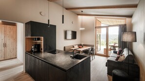 A modern kitchen with a central island, a dining area with a table and chairs, and a sofa. - Oberplunerhof Luxury Chalet Skyline with Mountain Views, Private Terraces & Shared Garden (Kiens)
