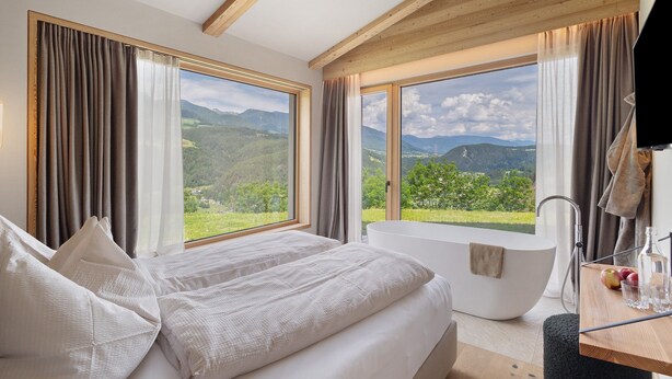 A bedroom with a large bed, a bathtub, and a view of mountains. - Oberplunerhof Luxury Chalet Skyline with Mountain Views, Private Terraces & Shared Garden (Kiens)