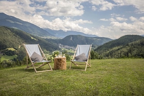 Deux chaises en bois avec des coussins, placées sur un champ herbeux avec vue sur la montagne.