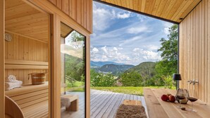 A wooden cabin with a sauna, a wooden deck, and a table with wine glasses and apples. - Oberplunerhof Luxury Chalet Skyline with Mountain Views, Private Terraces & Shared Garden (Kiens)