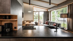 Een moderne keuken met een ingebouwde koffiezetapparaat, een eethoek met een tafel en stoelen, en een woongedeelte met een bank en een groot raam.