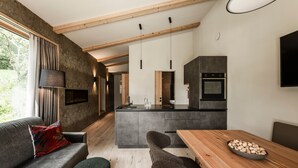 Een moderne keuken met een centraal eiland, een eethoek met een houten tafel, en een woonkamer met een bank en poef.