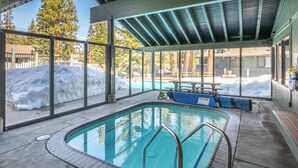 Piscina interior com paredes de vidro transparente, teto coberto e vista para área externa coberta de neve.