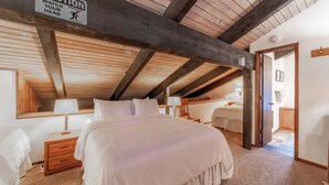 Quarto com teto de madeira, placa de aviso, cama, mesa de cabeceira e luminária.
