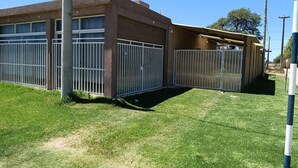A building with a garage and a covered area, surrounded by a white metal fence. - BellaVilla (Bell Ville)