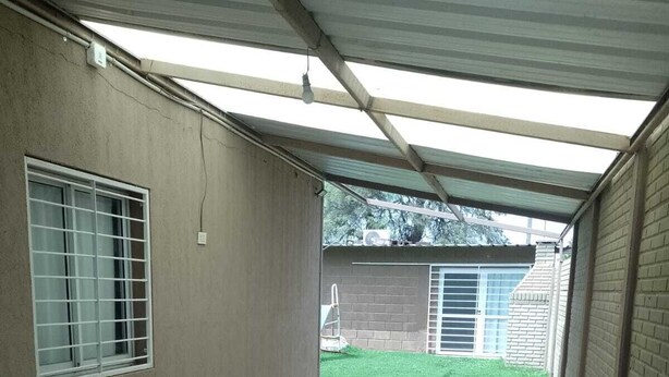 A covered outdoor area with a tiled floor, a window with bars, and a view of a grassy yard. - BellaVilla (Bell Ville)