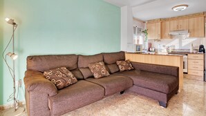 Ein Wohnzimmer mit einer Couch, einer Stehlampe und einer Küchenzeile mit Schränken und Geräten.