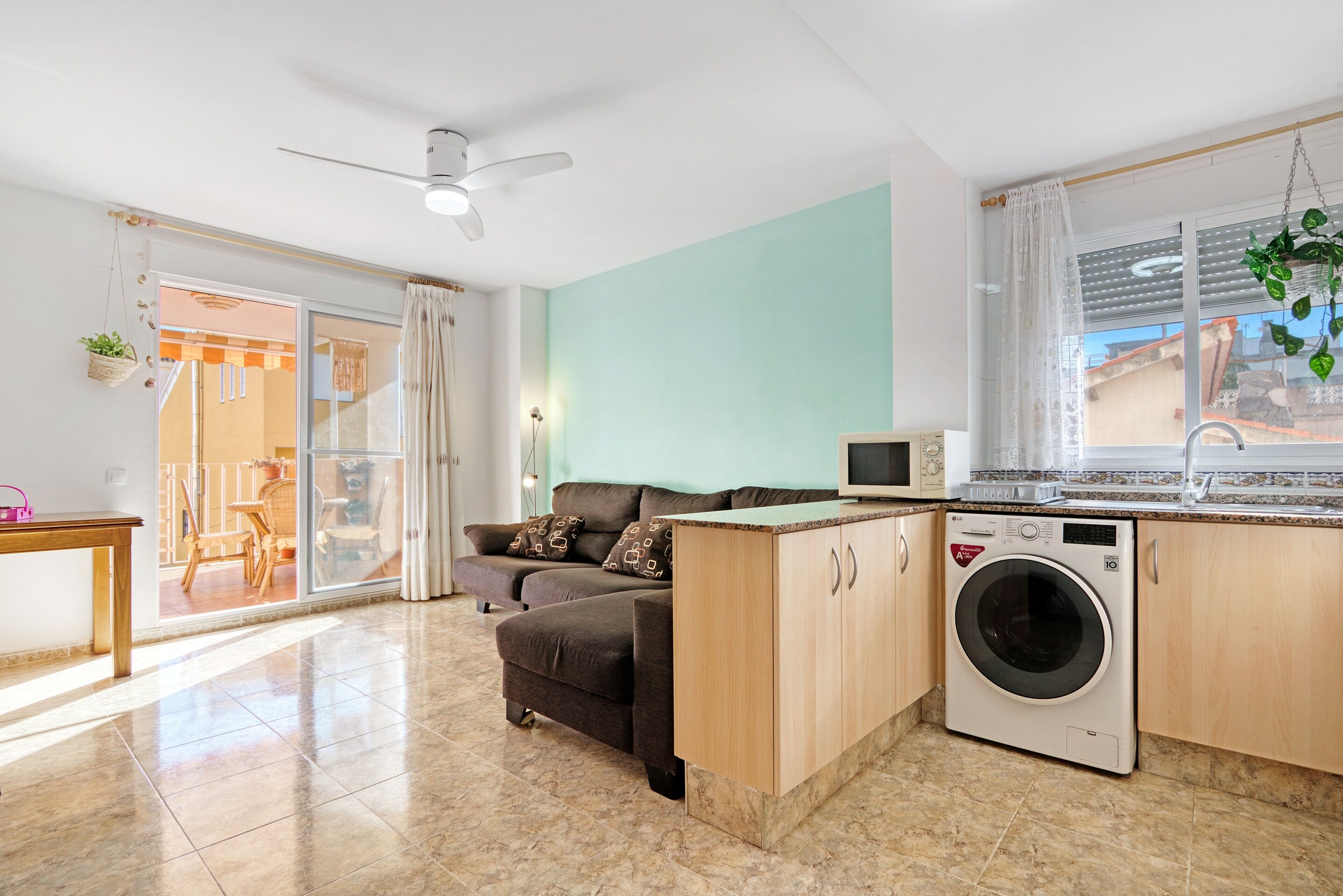 Un apartamento moderno con sofá, lavadora, ventilador de techo y vistas al exterior.