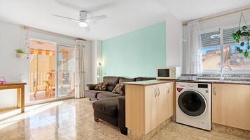 Un apartamento moderno con sofá, lavadora, ventilador de techo y vistas al exterior.