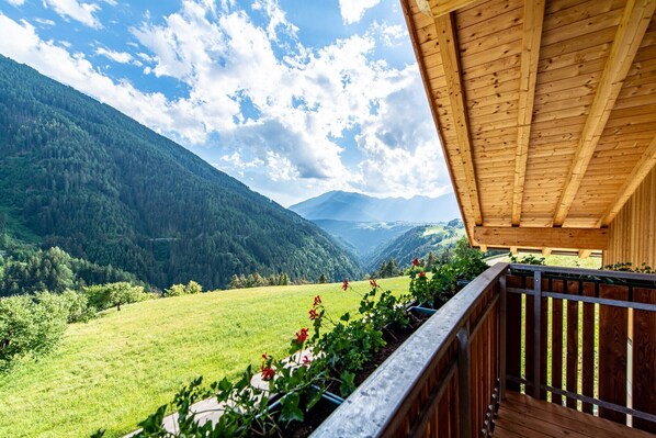A wooden balcony with a view of a valley and mountains.