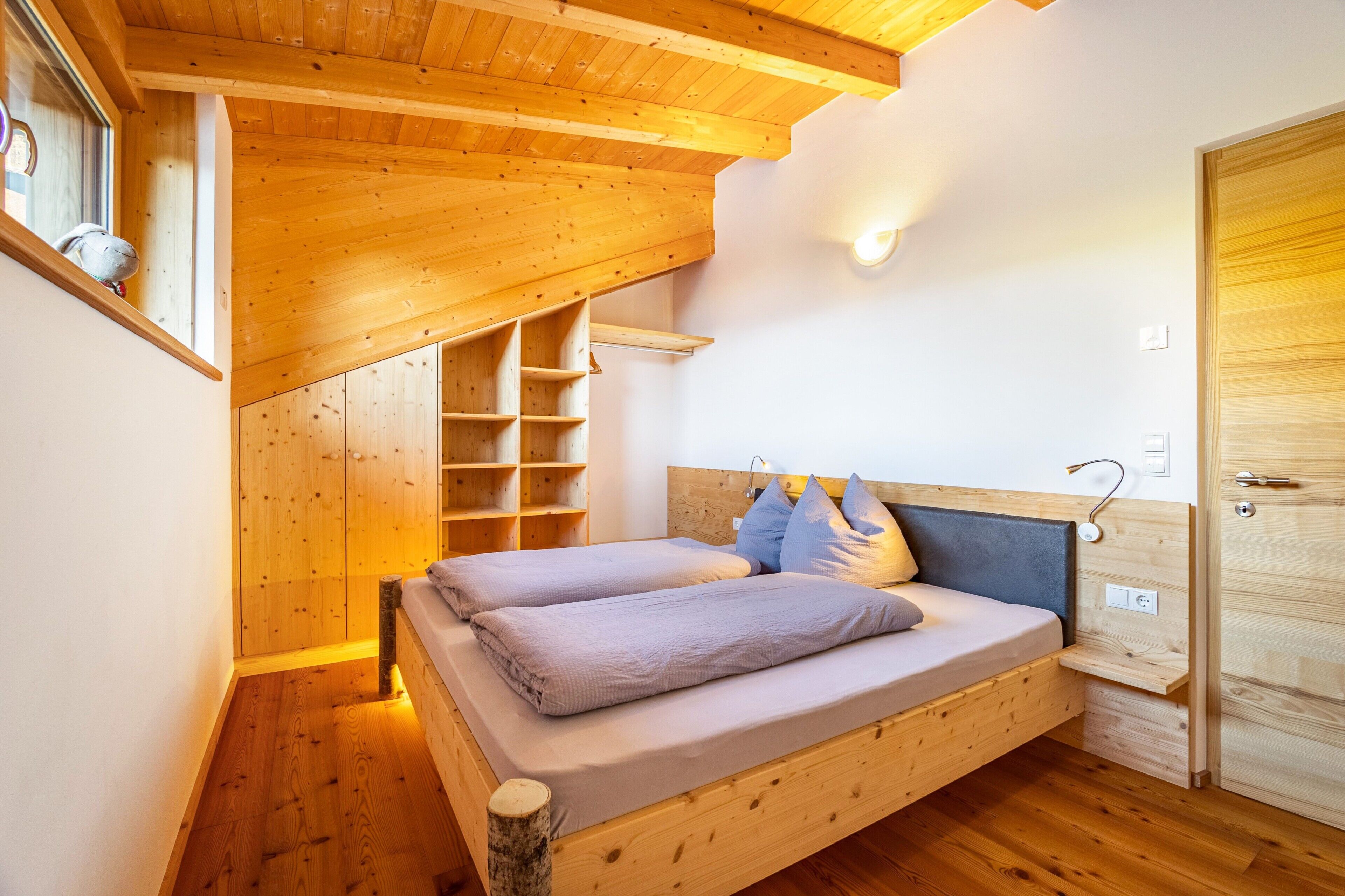 A wooden room with a bed, a wooden shelf, and a door.