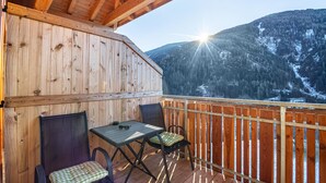 A wooden deck with a table and chairs, overlooking a mountainous landscape.