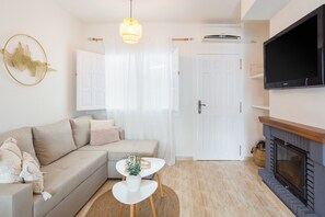 A living room with a sofa, a small white table, a fireplace, a TV, and a door.
