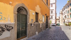 A narrow cobblestone street with a building featuring a green door and a sign indicating a public telephone. - Milo Apt - Trastevere's Gem (Roma)