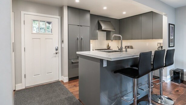 Une cuisine moderne avec des meubles gris, un plan de travail blanc et un coin bar avec des tabourets.