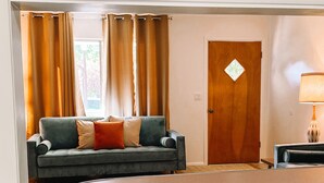 A living room with a sofa, curtains, a wooden door, and a lamp.