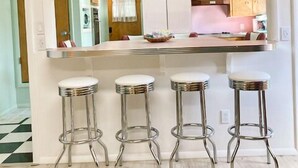 A modern kitchen with a flat-screen TV, a countertop with bar stools, and a visible sink.