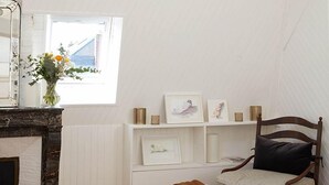 Ein Schlafzimmer mit schrägen Wänden, Kamin, Bett, Nachttisch, Sessel und einem Fenster mit Blick.