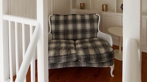 A cozy room with a checkered sofa, wooden flooring, and white paneled walls.